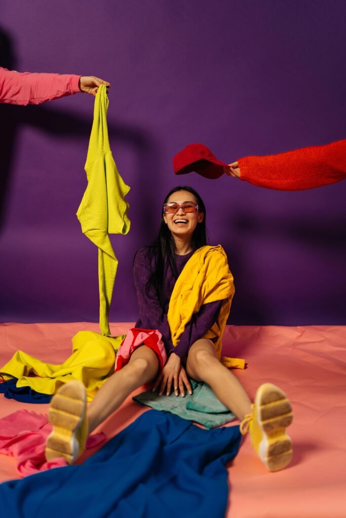 Woman in colorful clothing sitting on a floor with bright fabrics against a purple background.